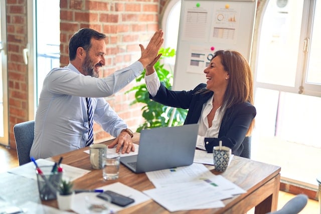 Two business professionals high fiving in front of a desk.